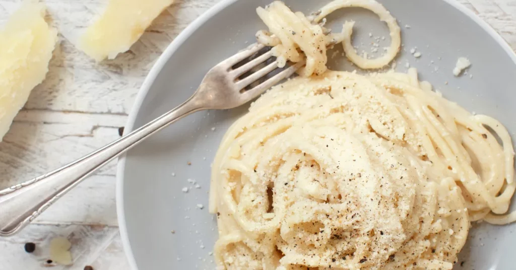 A close-up image showing the creamy and rich Cacio e Pepe sauce, perfectly coating the pasta, with visible grains of freshly ground black pepper, highlighting the authentic Italian flavors.