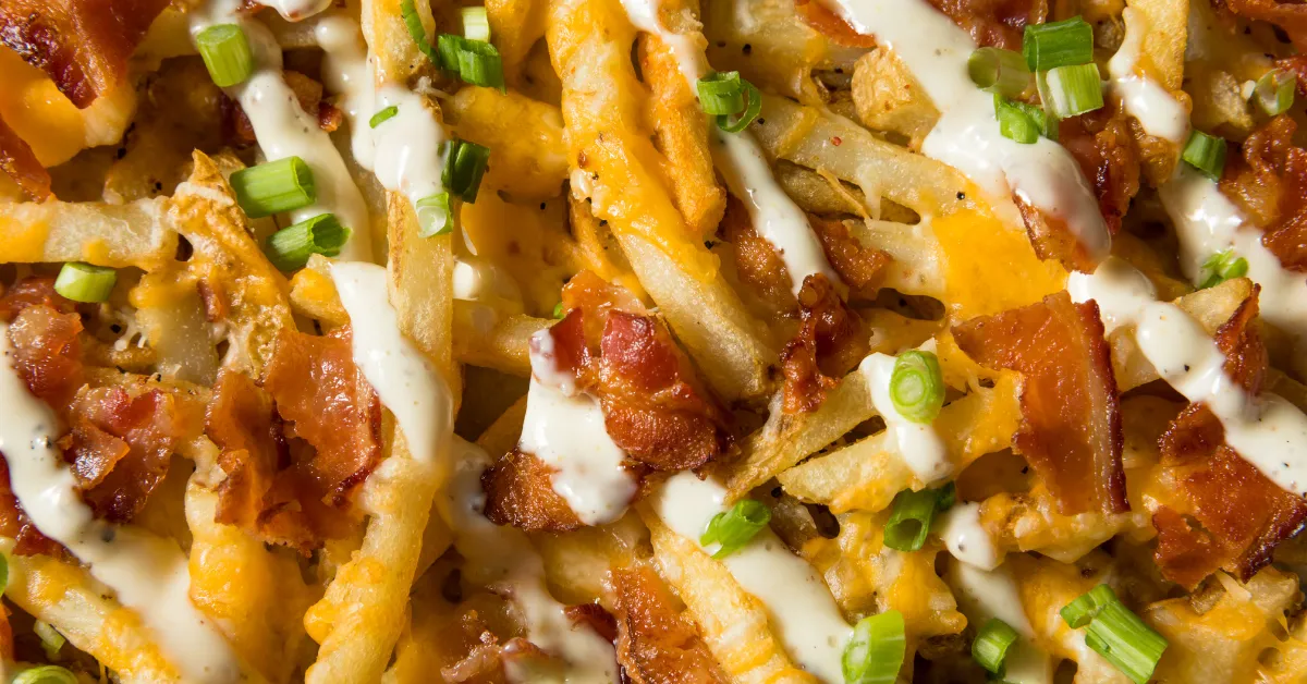 A close-up of a plate of french fries with cheese, bacon, and ranch dressing, with the article titled "Crack Chicken Name Debate" in the background.