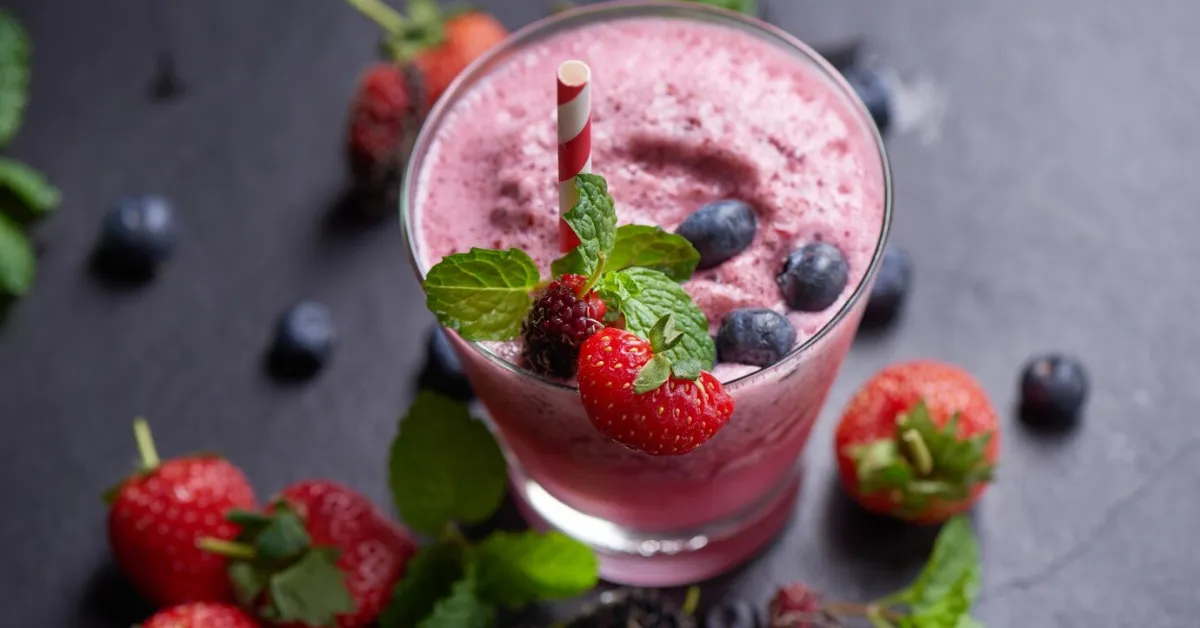 A frozen fruit smoothie in a glass, garnished with fresh berries and mint.