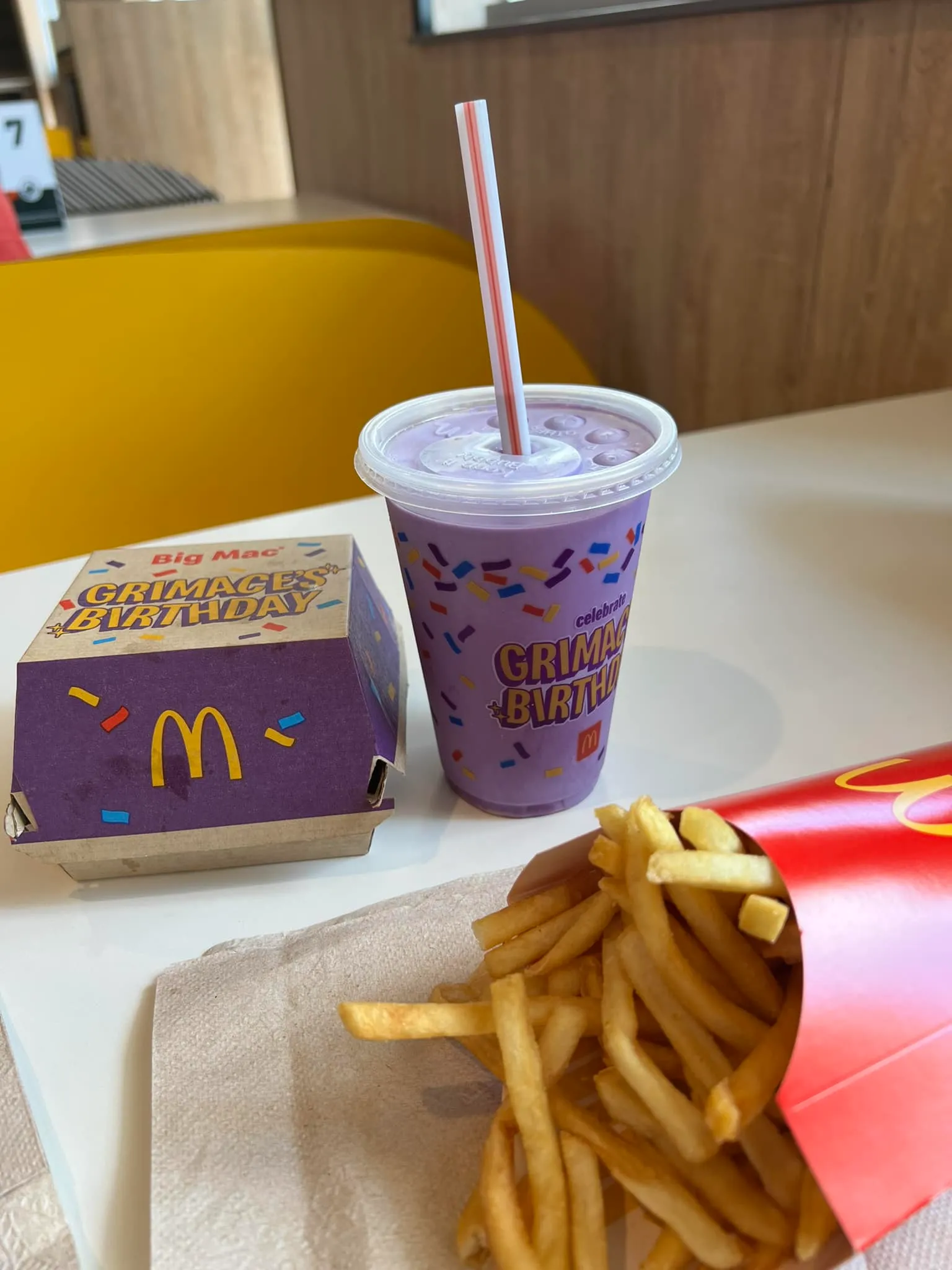 Grimace Shake on a table with Mcdonald's burger and potatoes.