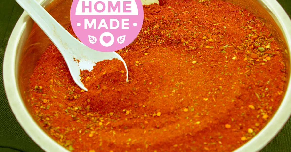 A bowl of chili powder with a spoon in it, representing a key ingredient in Trim Healthy Mama Homemade Cajun Seasoning.