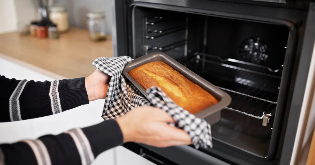 How long to bake a cake? Close-up of a person taking a loaf of bread out of an oven.