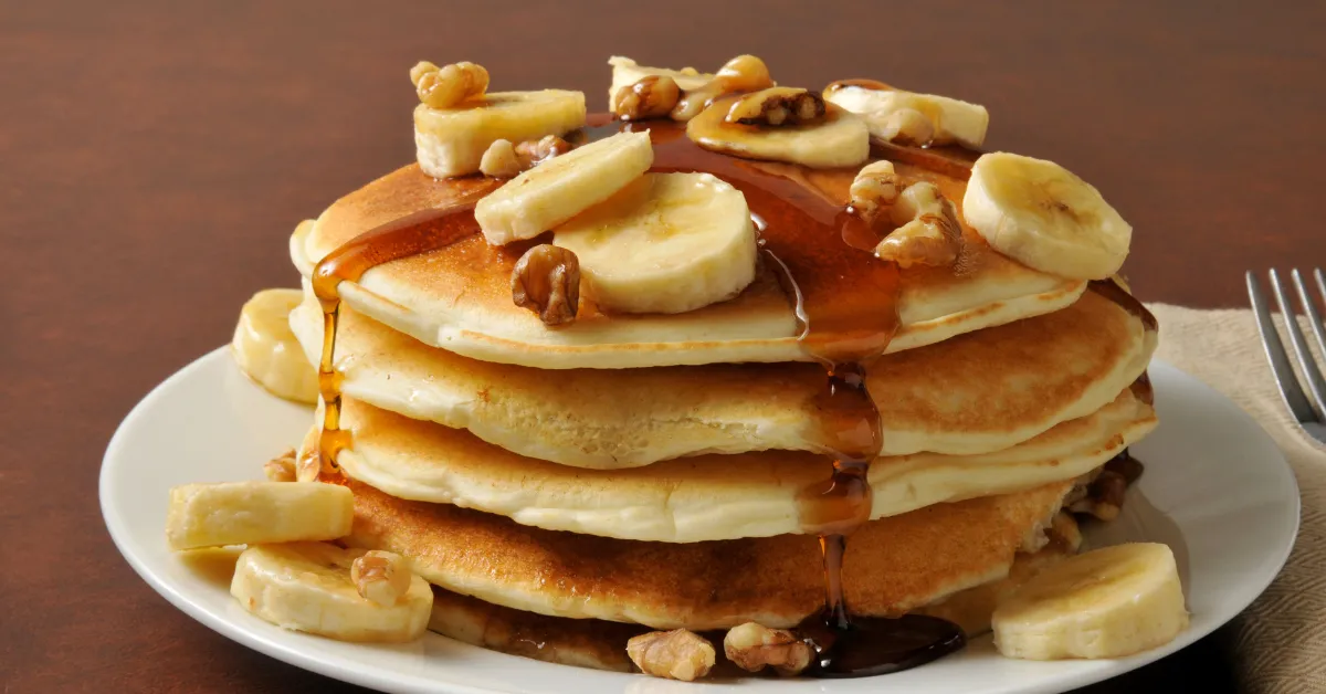 Pile of amangiri pancake with banana and maple syrup on its top