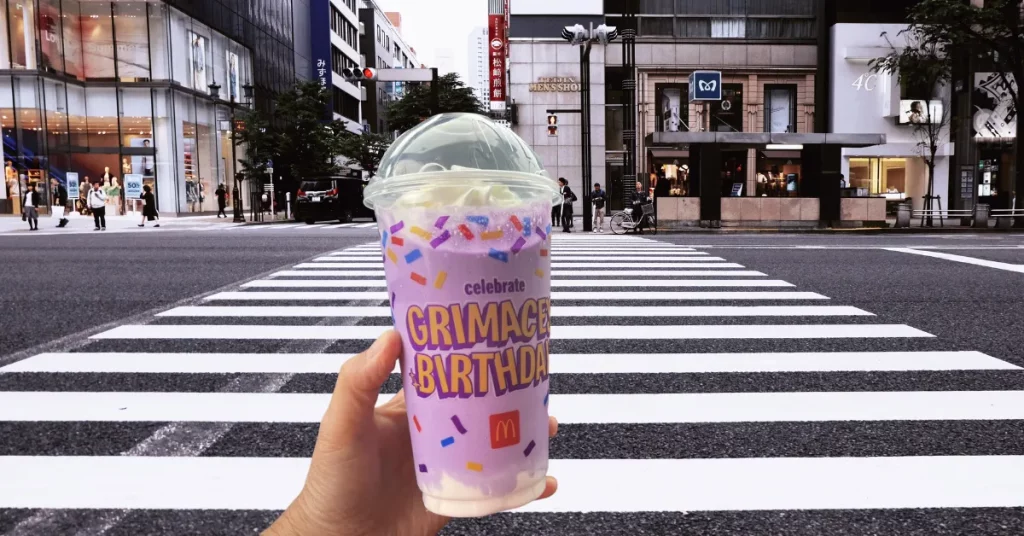 A hand holding Grimace Birthday Shake in a street