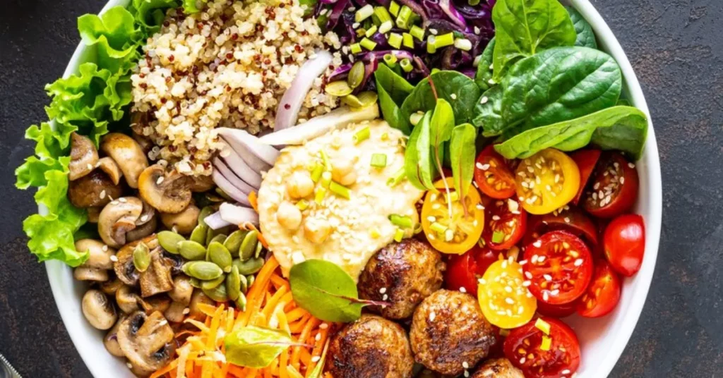 Bowl of vegetarian food, including vegetables, meatballs, rice, and hummus.