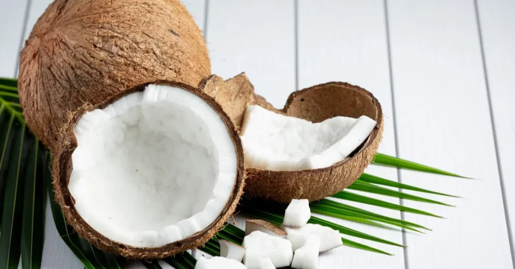 Two coconuts sitting on a wooden table, one whole and one cracked open.