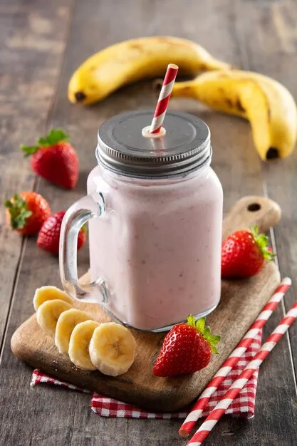 A strawberry banana smoothie in a mason jar, garnished with a strawberry slice and a banana slice.