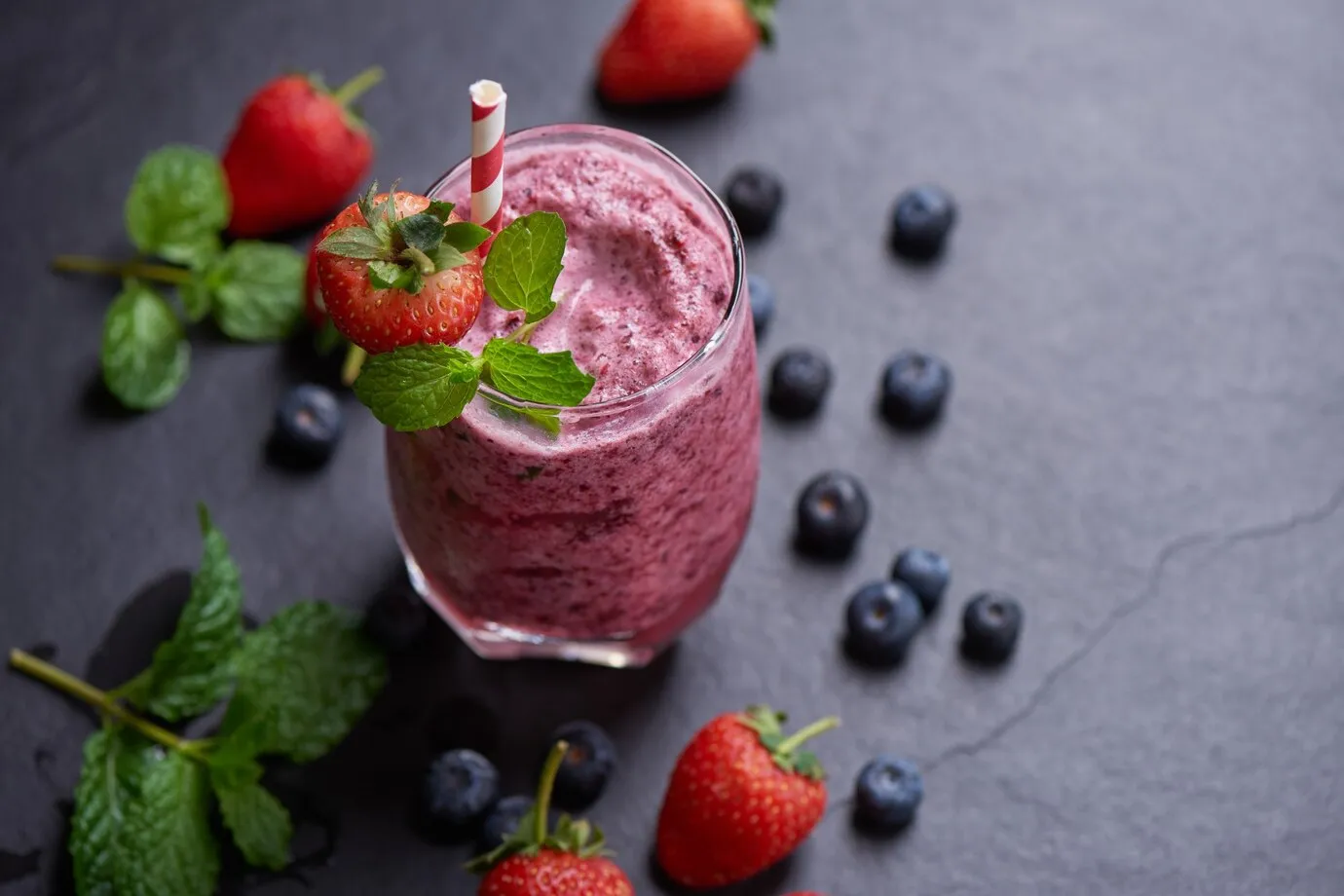 delicious strawberry, mulberry and blueberry smoothie garnished with fresh berries and mint in glass