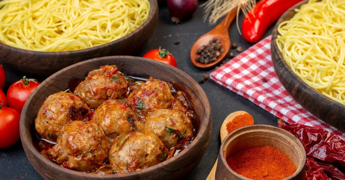 A bowl of spaghetti and meatballs on a wooden table. The spaghetti is cooked in a tomato sauce and the meatballs are browned.