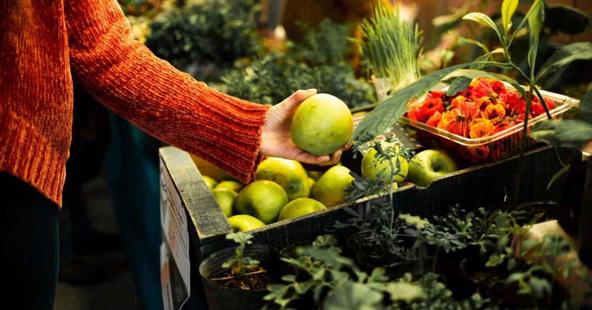 Daily Harvest offers a variety of fresh, plant-based meals at affordable prices. (Image: A person reaching for a fresh, green apple at a farmers market stall.)