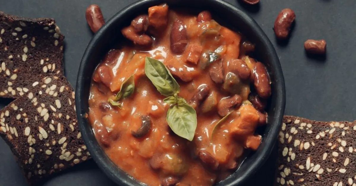 A bowl of baked beans in a tomato sauce next to crackers. Mustard is a popular condiment that is often used in baked beans because it adds a tangy flavor and helps to cut through the richness of the dish.