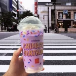 A hand holding Grimace Birthday Shake in a street