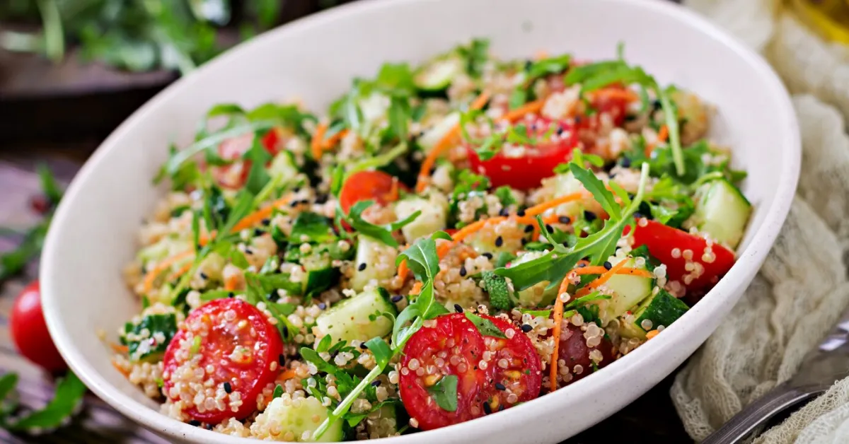 A bowl of quinoa salad with tomatoes, cucumbers, arugula, and sesame seeds. Quinoa is a good source of protein, but it's also low in calories and fat. This salad is a healthy and delicious way to get 100g of protein without meat.