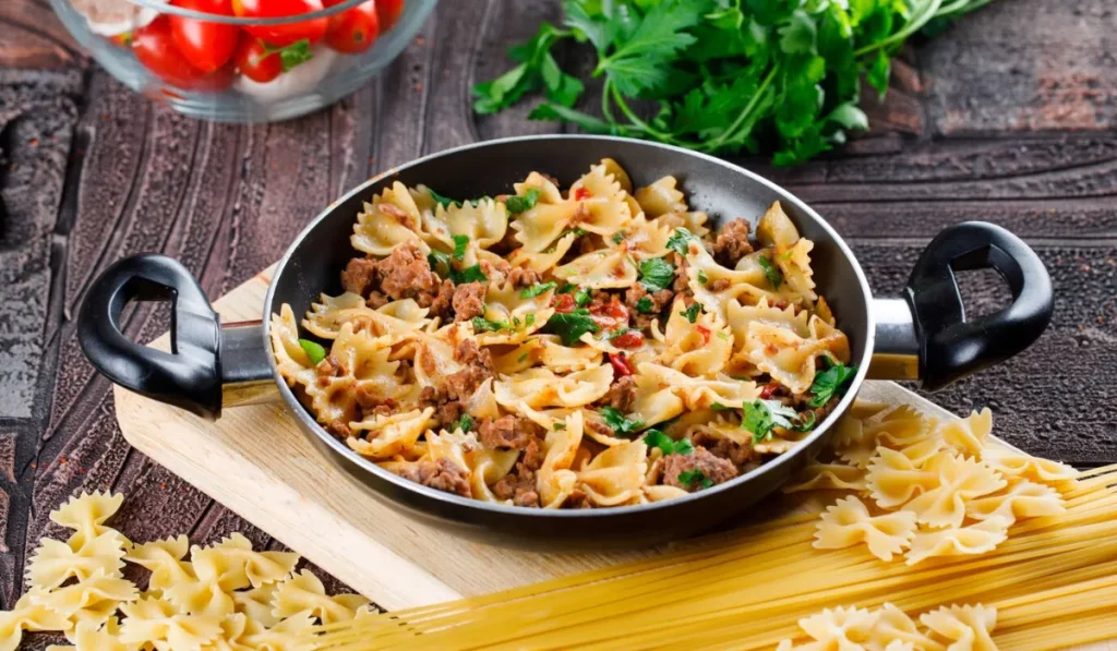 Louisiana Chicken Pasta meal in pan with raw pasta, mushroom, parsley, tomato which is high in calories
