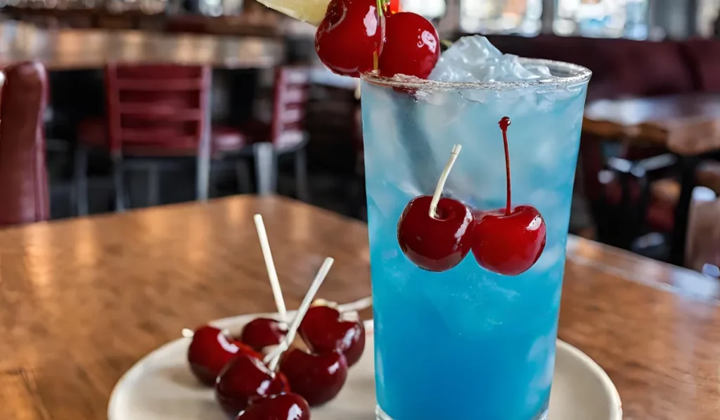A refreshing blue cocktail, kenny chesney cooler recipe, in a tall glass with a straw and cherry on top, sitting on a wooden table